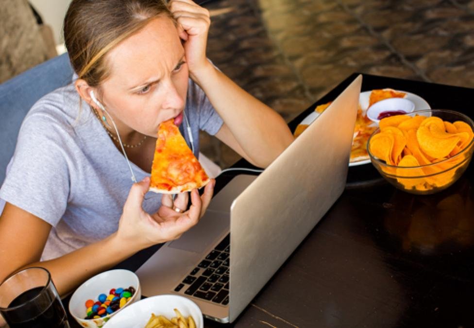 une personne qui mange tout en étant absorbée par son ordinateur.
